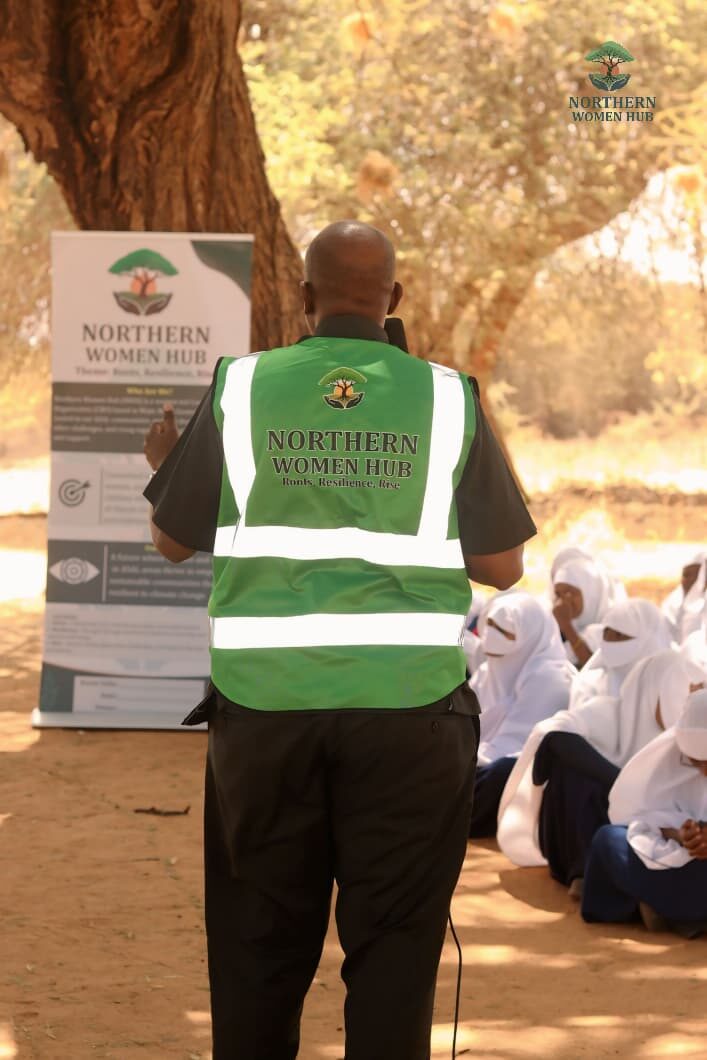 Northern Women Hub team member briefing a group of schoolgirls under an acacia tree in the field