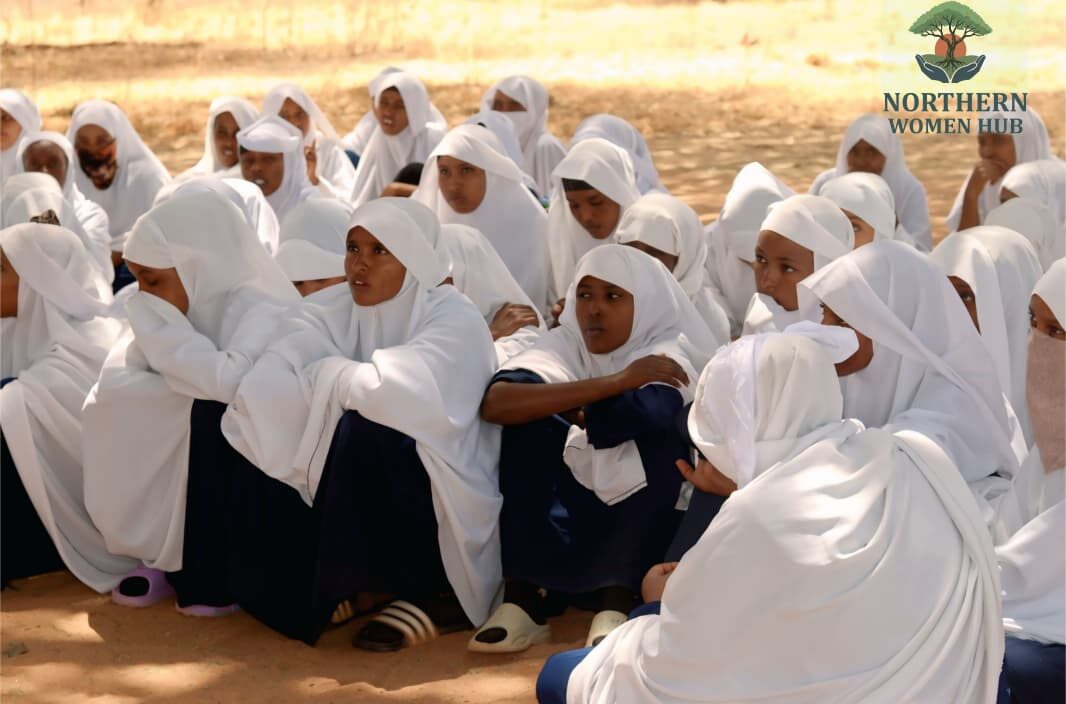 Girls in white school hijabs sitting together in a circle under a tree during a Northern Women Hub community session in Wajir